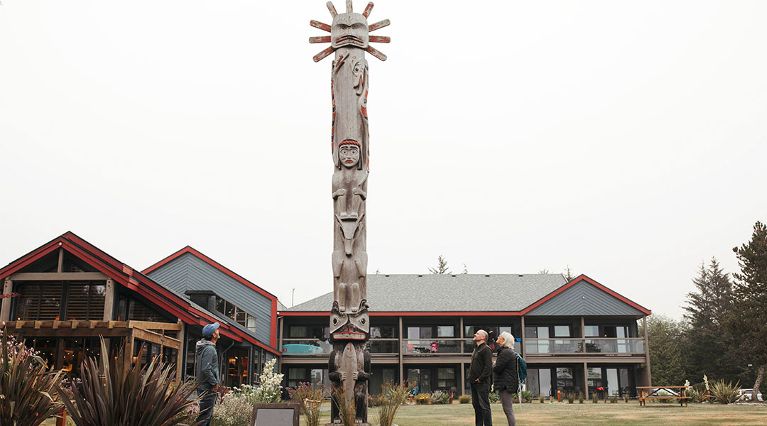 Exterior photo of hotel with people looking at totem pole 