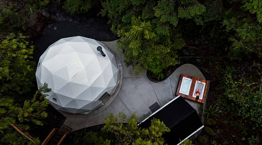 Aerial view of a white geodesic dome surrounded by dense forest
