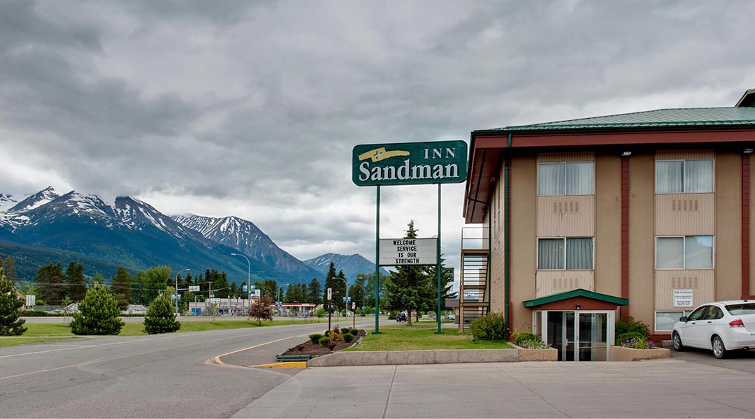 The exterior building and sign of the Sandman Inn Smithers near snowcapped mountains in Northern BC