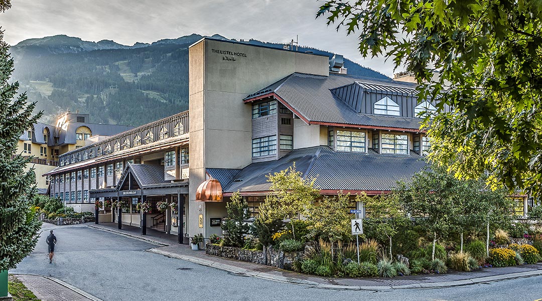 The exterior building and entrance to The Listel Hotel Whistler with a tall mountain backdrop