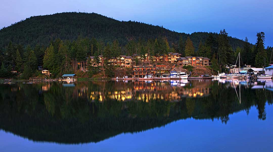 Exterior of the Painted Boat Resort Spa and Marina with the mountains and resort reflection off the water in Madeira Park