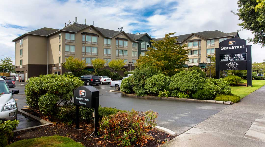 Exterior of the Sandman Hotel in Victoria with parking lot out front of entrance
