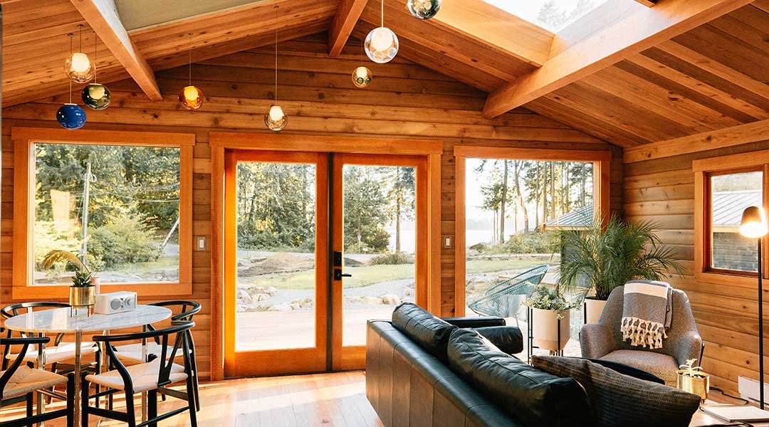 The living area and dining table with large windows in a wooden cabin at the Bodega Cove on Galiano Island