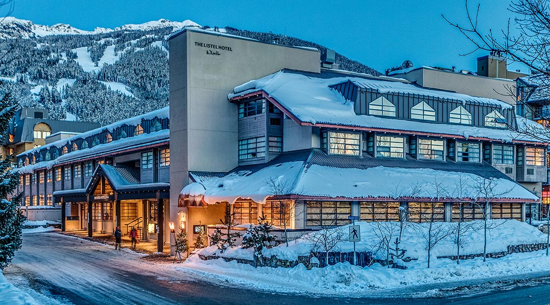 The exterior building and entrance to The Listel Hotel Whistler covered in snow during winter