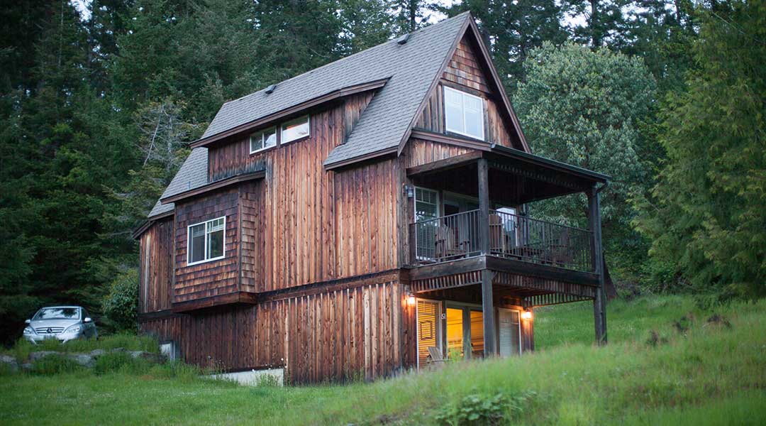 The exterior of a wooden cottage with a parked car in the evening at the Cottages on Salt Spring Island
