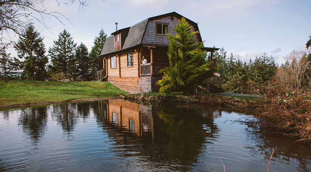 Person relaxing on the balcony of a wooden cabin near a lake at the Bodega Ridge on Galiano Island