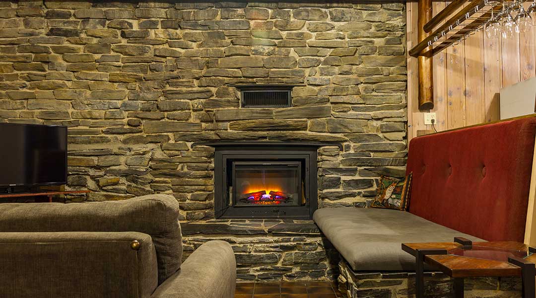 Fireplace in dark brick wall near sofa and TV in the lodge suite at the Bella Coola Mountain Lodge