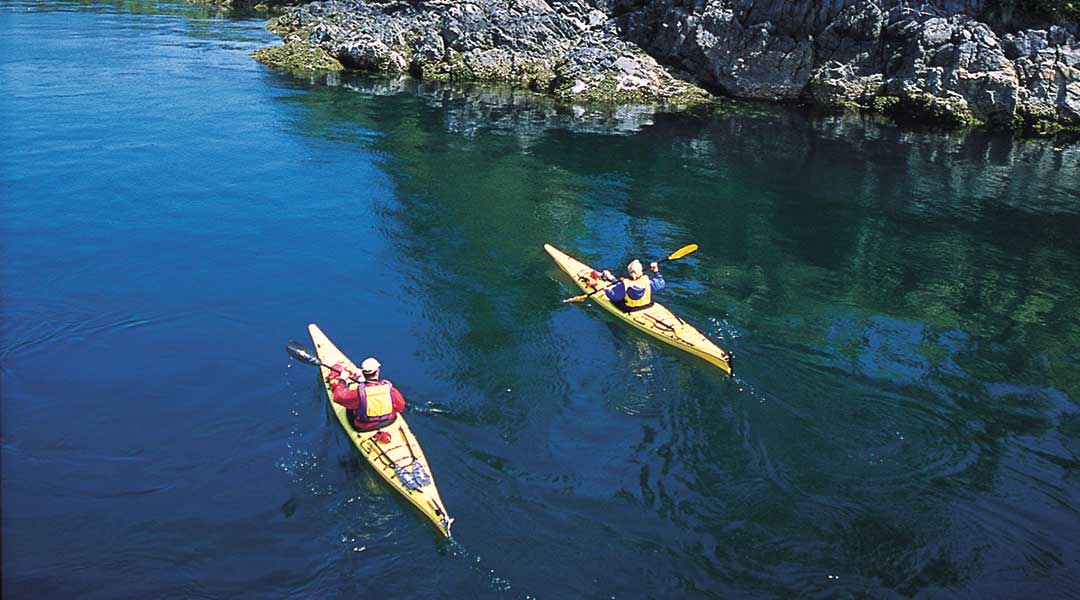 Two kayakers kayaking next to rocky bluffs near the Brentwood Bay Resort and Spa on Vancouver Island