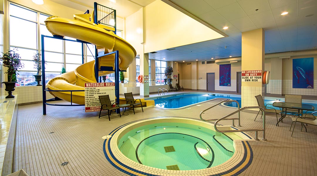 The swimming pool area with a hot tub and waterslide at the Prestige Treasure Cove Hotel in Prince George
